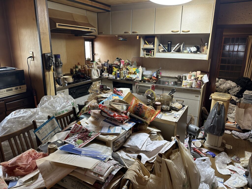 京都市伏見区の4LDK一軒家。片付け前の台所で、テーブルや床に生活用品が置かれている様子。